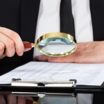 Businessman Analyzing Document With Magnifying Glass At Desk
